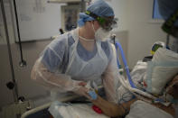 A nurse holds the hand of a COVID-19 patient on a ventilator in the COVID-19 intensive care unit at the la Timone hospital in Marseille, southern France, Friday, Dec. 31, 2021. Paris region health authorities have instructed hospitals to cancel more non-urgent medical procedures to free up intensive-care beds for the growing influx of people gravely sick with COVID-19. (AP Photo/Daniel Cole)