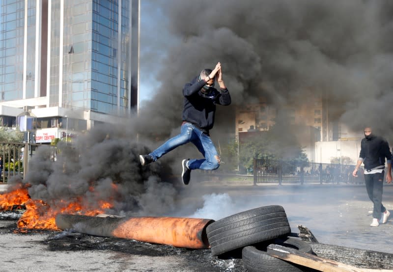 A protestor jumps over a burning barricade during a protest over economic hardship and lack of new government in Beirut