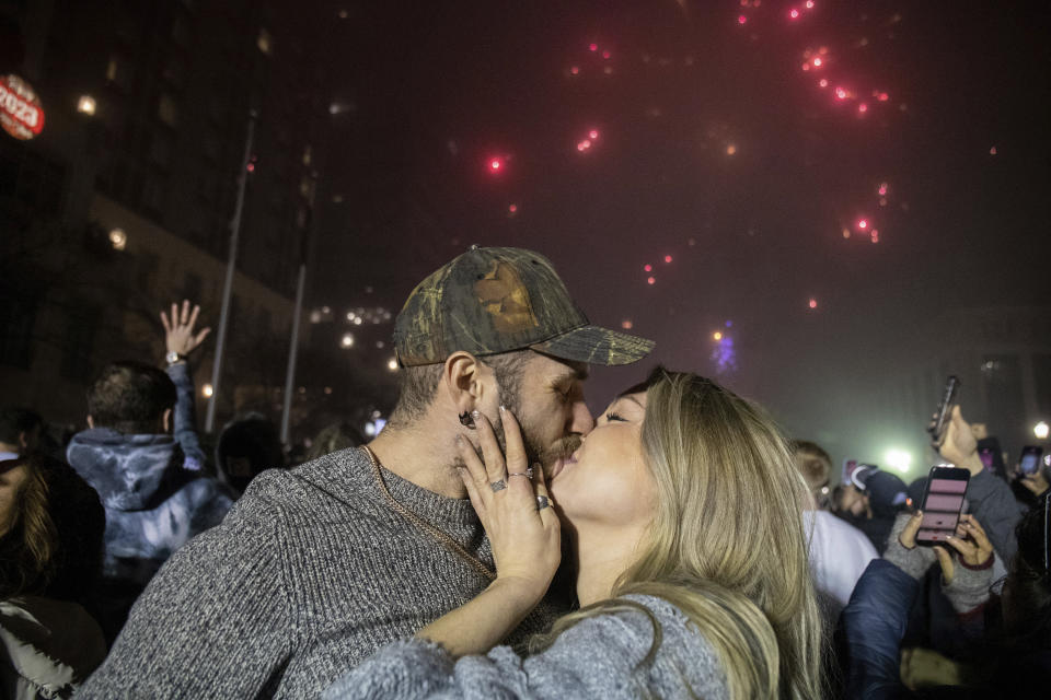 Hagan Schenck and Maddi Showalter share a kiss after the Strawberry drops, upper left, and fireworks explode in Market Square to ring in the New Year, in Harrisburg, Pa., Sunday, Jan. 1, 2023. (Mark Pynes/The Patriot-News via AP)