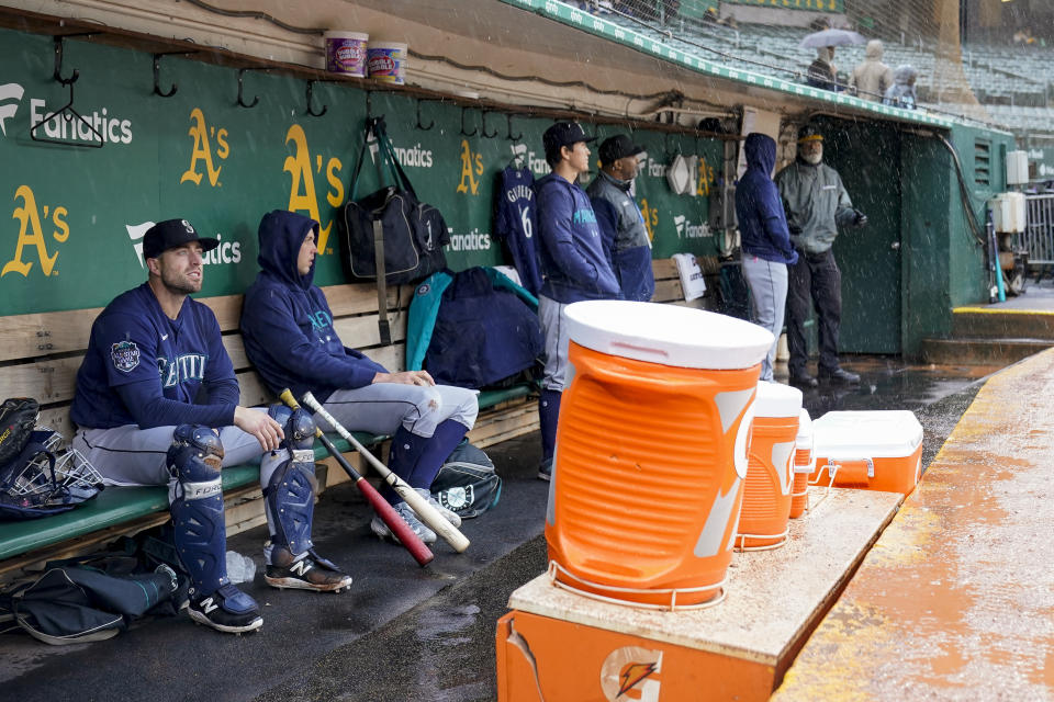 Seattle Mariners catcher Tom Murphy, left, sits in the dugout as rainfall causes a weather delay before a baseball game between the Oakland Athletics and Mariners in Oakland, Calif., Wednesday, May 3, 2023. (AP Photo/Godofredo A. Vásquez)