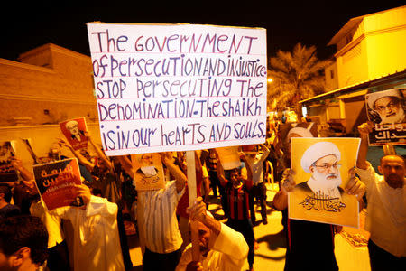 A protester holds a sign that reads "The government of persecution and injustice. Stop persecuting the denomination. The sheikh is in our hearts and souls" and photos of Bahrain's leading Shi'ite cleric Isa Qassim during a sit-in outside his home in the village of Diraz west of Manama, Bahrain July 27, 2016. Qassim went on trial on Wednesday on charges of collecting donations illegally and money laundering. REUTERS/Hamad I Mohammed