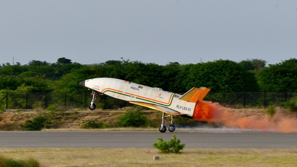 a white airplane with no windows or cockpit canopy lands on a runway surrounded by tropical vegetation