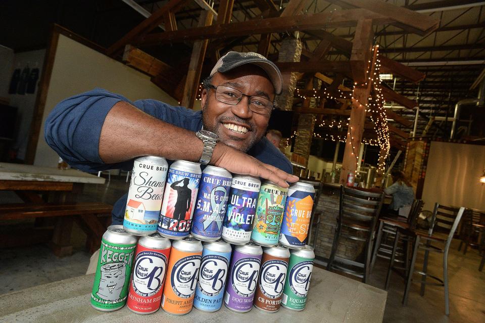 Kevin Merritt, owner and brewer of Crue Brew in Raynham, poses with cans of his beers on Thursday, Sept. 2, 2021.