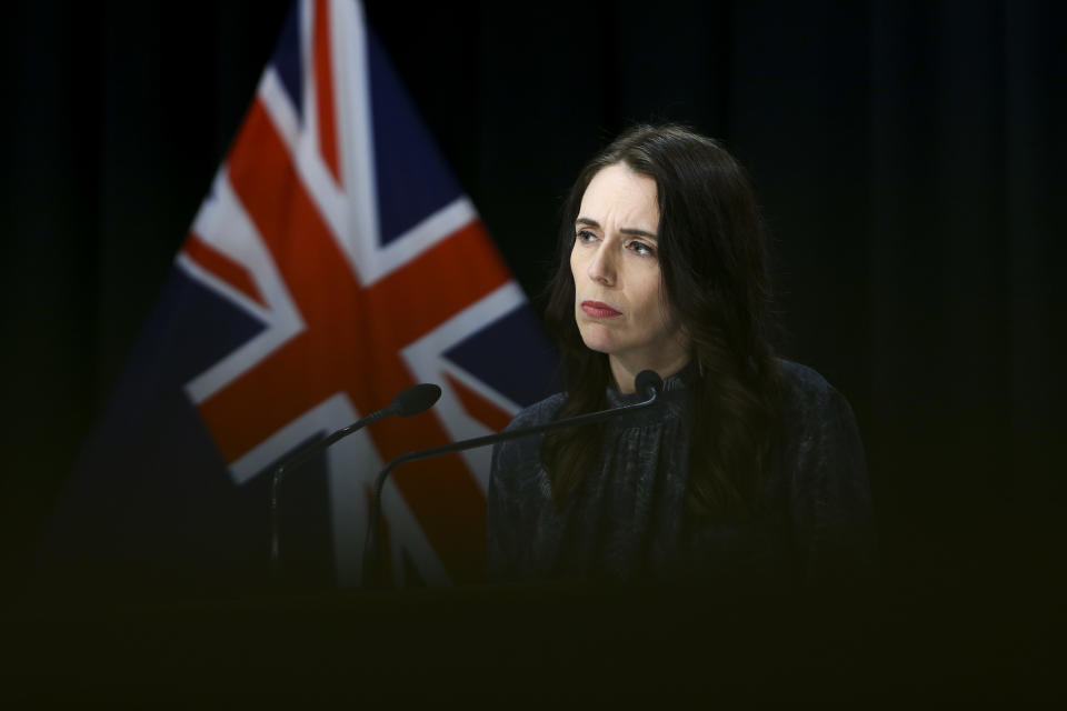 Jacinda Ardern pictured in all black in front of a New Zealand flag.