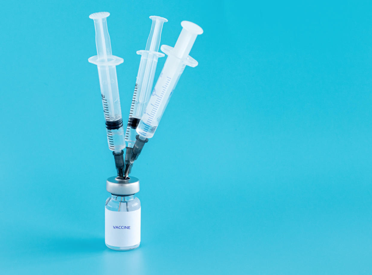 Bottle of vaccine, and three medical needles with injections stuck in the bottle cap on a blue isolated background. Vaccination against the flu, infections, covid-19. Copy space. Selective focus