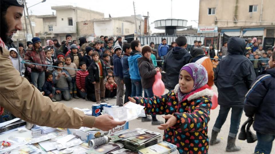 Islamic State militant, left, distributes soft drinks, candy, biscuits along with religious pamphlets to a Syrian young girl, right, during a street preaching event in Tel Abyad in Raqqa province, northeast Syria. Photo: AP