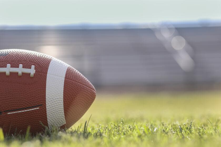 Football on grass stadium on college or high school campus. Bleachers background. No people. Daytime.