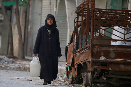 A woman carries a container of water as she walks past a burnt pick-up truck in the rebel held area of Old Aleppo, Syria November 14, 2016. REUTERS/Abdalrhman Ismail/File Photo