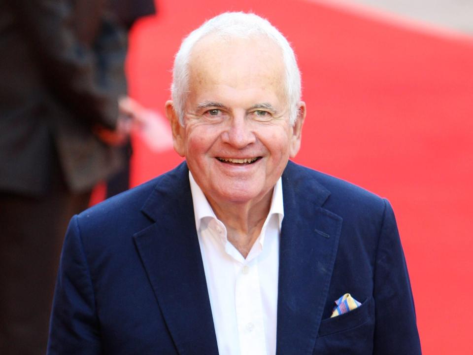 Ian Holm wearing a blue suit and white button up on red carpet