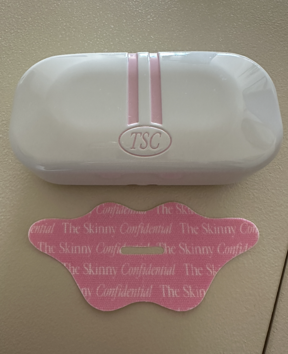 A TSC branded case with a matching lip-shaped face tape below it, both with "The Skinny Confidential" text