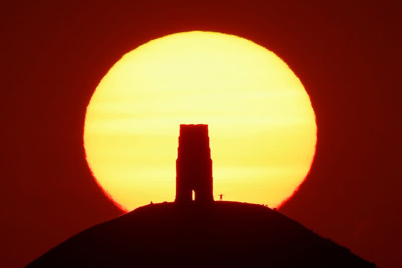FILE PHOTO: A person views the sun rise from beside the remains of Saint Michael's Church on top of Glastonbury Tor, in Glastonbury
