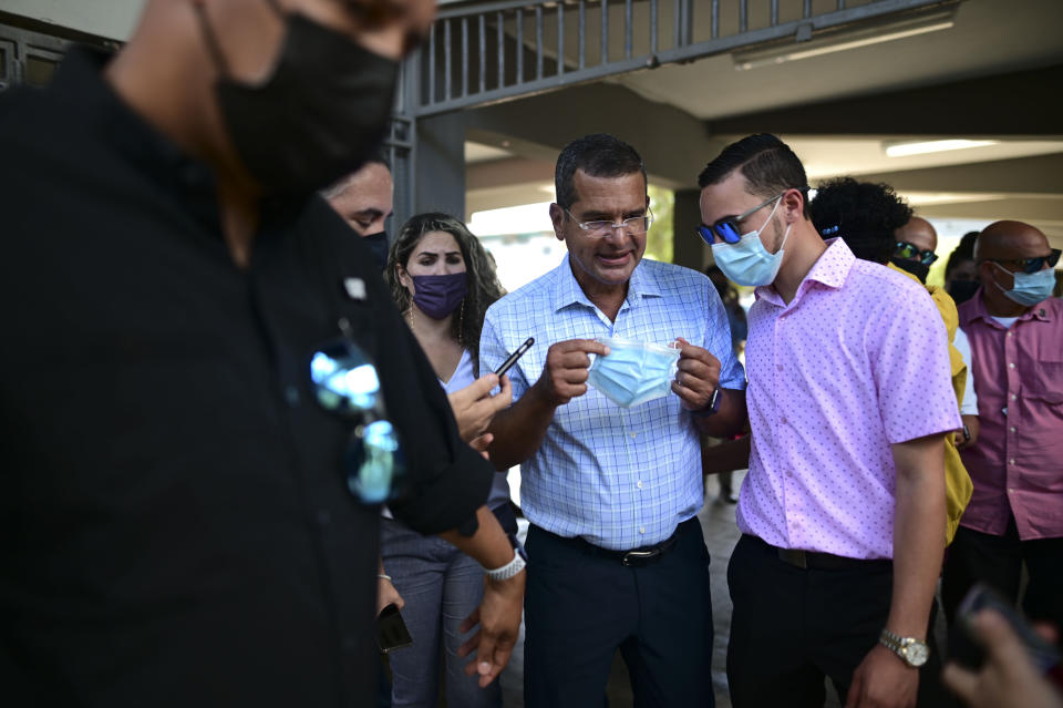 FILE - In this March 10, 2021 file photo, Puerto Rico Gov. Pedro Pierluisi, center, attends a mass vaccination campaign against COVID-19 at the Maria Simmons elementary school in Vieques, Puerto Rico. Pierluisi has resisted tighter restrictions, saying another lockdown would be too extreme and that things will keep improving and the island could achieve herd immunity by August 2021: “The solution is vaccination.” (AP Photo/Carlos Giusti, File)