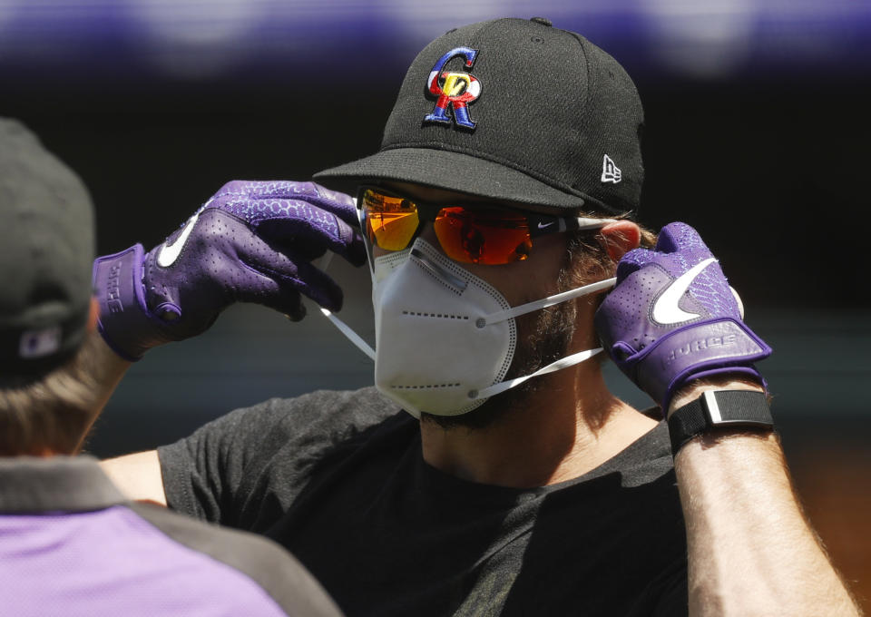 Colorado Rockies left fielder David Dahl puts on a face mask while taking part in drills as the team practiced Wednesday, July 8, 2020, in Denver. (AP Photo/David Zalubowski)