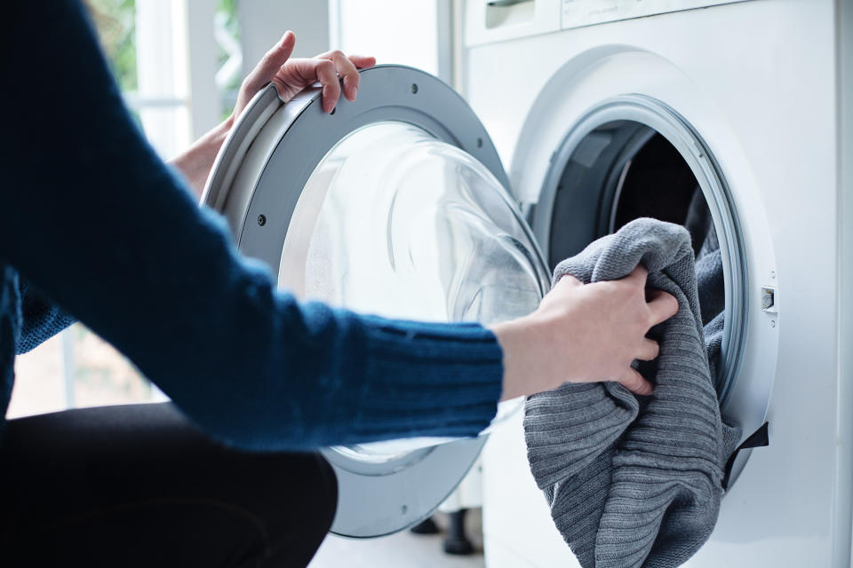 Woman’s hand loading dirty laundry in a white washing machine
