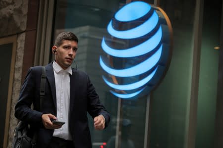 FILE PHOTO: A man uses his phone as he passes by an AT&T store on Wall St. in New York
