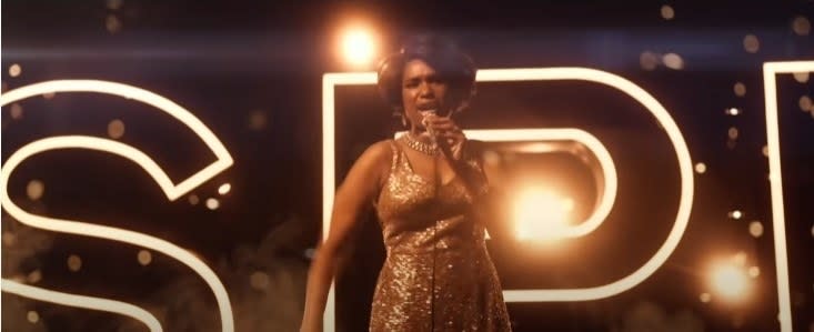 Jennifer Hudson as Aretha Franklin, wearing a gold sequinned sleeveless dress and singing on stage in front of illuminated golden letters spelling out "respect"