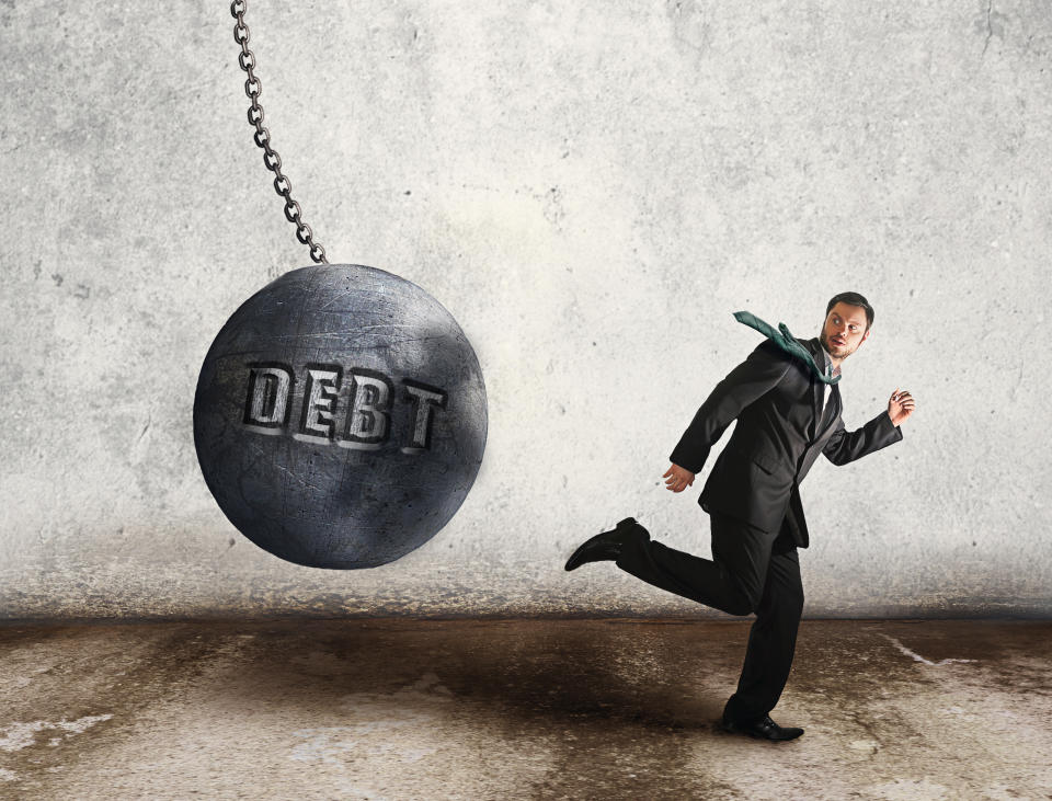 Businessman running from a giant ball on a chain with the word debt engraved on it