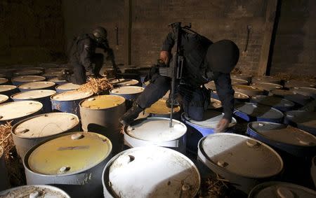 Federal policemen look at seized barrels they suspect contain the ingredients to make crystal methamphetamines during an operation against the Michoacan cartel known as "La Familia" (The Family) in Apatzingan in Mexico's state of Michoacan, in this October 29, 2009 file photo. REUTERS/Daniel Aguilar/Files