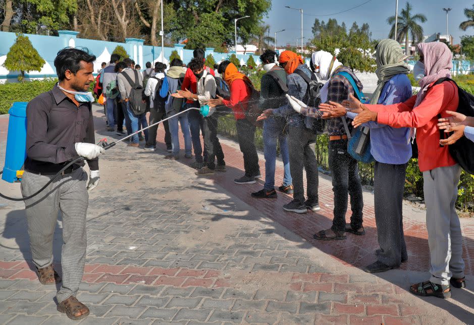 A municipal worker sprays disinfectant on migrant workers in Lucknow before they board a bus to return to their villages.