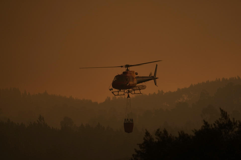 A firefighting helicopter flies low through thick smoke from a forest fire in the village of Bemposta, near Ansiao, central Portugal, Wednesday, July 13, 2022. Thousands of firefighters in Portugal continue to battle fires all over the country that forced the evacuation of dozens of people from their homes. (AP Photo/Armando Franca)