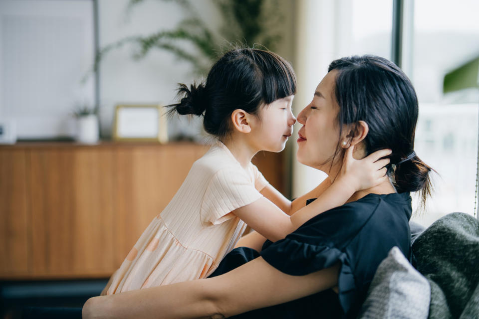 A mother and daughter lovingly touch noses in the living room