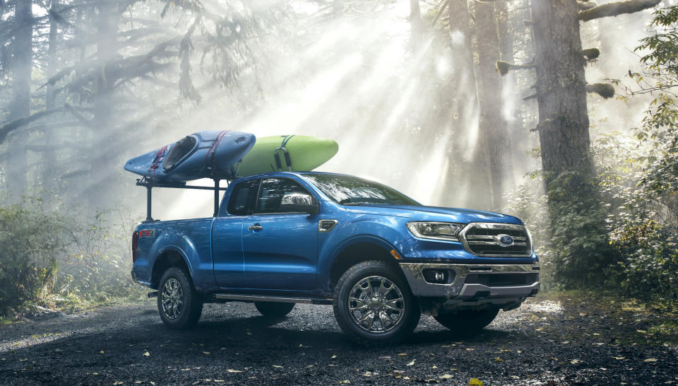 A blue 2019 Ford Ranger, a midsize pickup, is shown in a forest setting. There are two kayaks loaded on a rack in the Ranger's bed.