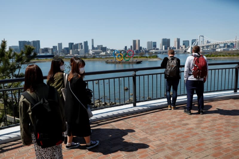 People wearing protective face masks due to the outbreak of coronavirus disease (COVID-19) walk and look in front of the Giant Olympic rings at the waterfront area at Odaiba Marine Park in Tokyo
