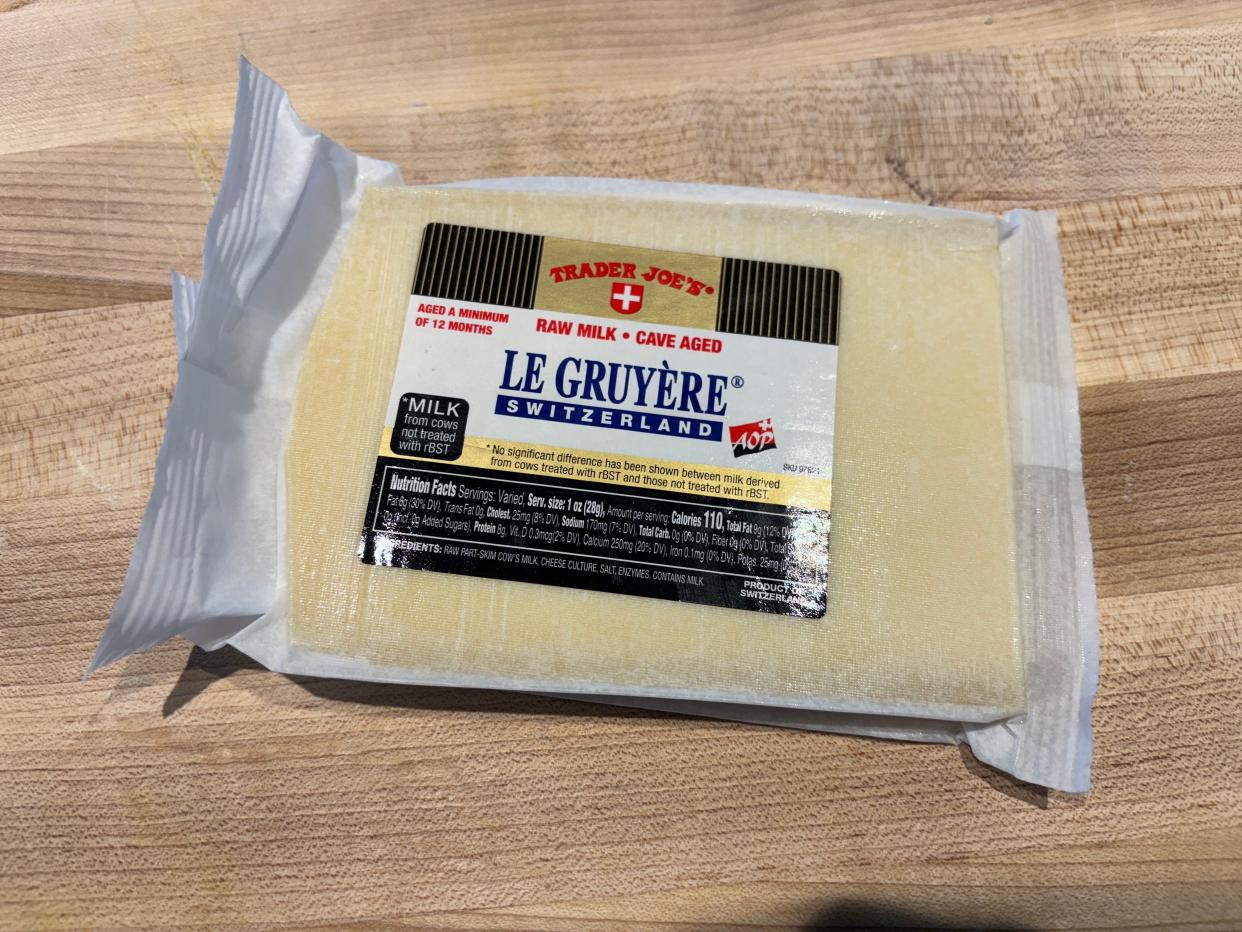 A rectangular package of Le Gruyere cheese with a black and white label on a wooden cutting board