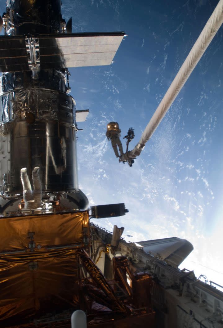 Mission Specialist John Grunsfeld is positioned on a foot restraint on the end of Atlantis' remote manipulator system and Andrew Feustel (top center), mission specialist, participate in the mission's fifth and final spacewalk. 