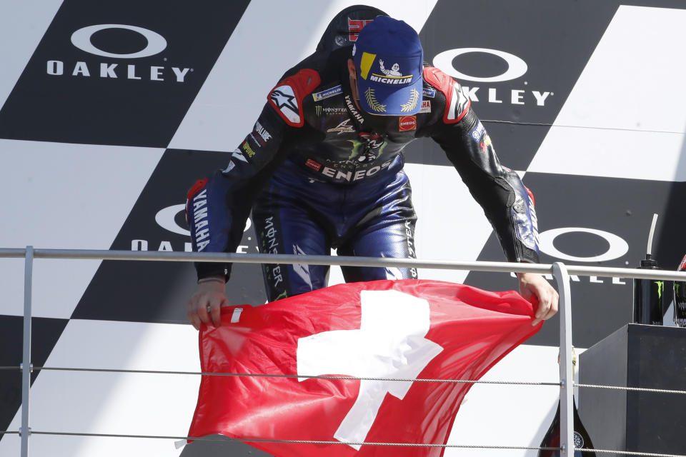 First placed, Yamaha rider Fabio Quartararo, of France, holds the Swiss flag to honor 19 years-old Swiss rider Jason Dupasquier, during the podium ceremony at the end of the Motogp Grand Prix of Italy at the Mugello circuit, in Scarperia, Italy, Sunday, May 30, 2021. Dupasquier died Sunday after being hospitalized Saturday, at the Florence hospital, following his crash during the qualifying practices of the Moto3. (AP Photo/Antonio Calanni)