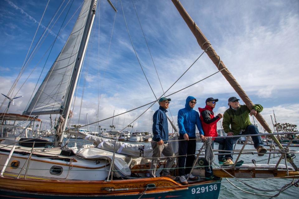 Four sailors pose on a yacht in a harbor
