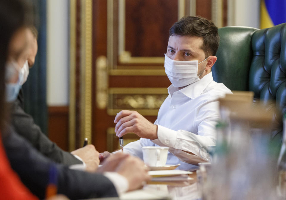 FILE - In this photo taken on Wednesday April 22, 2020, Ukrainian President Volodymyr Zelenskiy in a face mask to protect against coronavirus, discusses the COVID-19 situation in the country with officials in his office in Kyiv, Ukraine. Zelenskiy has switched to a special work mode as his wife Olena was tested positive for the coronavirus, his office said. (Ukrainian Presidential Press Office via AP)