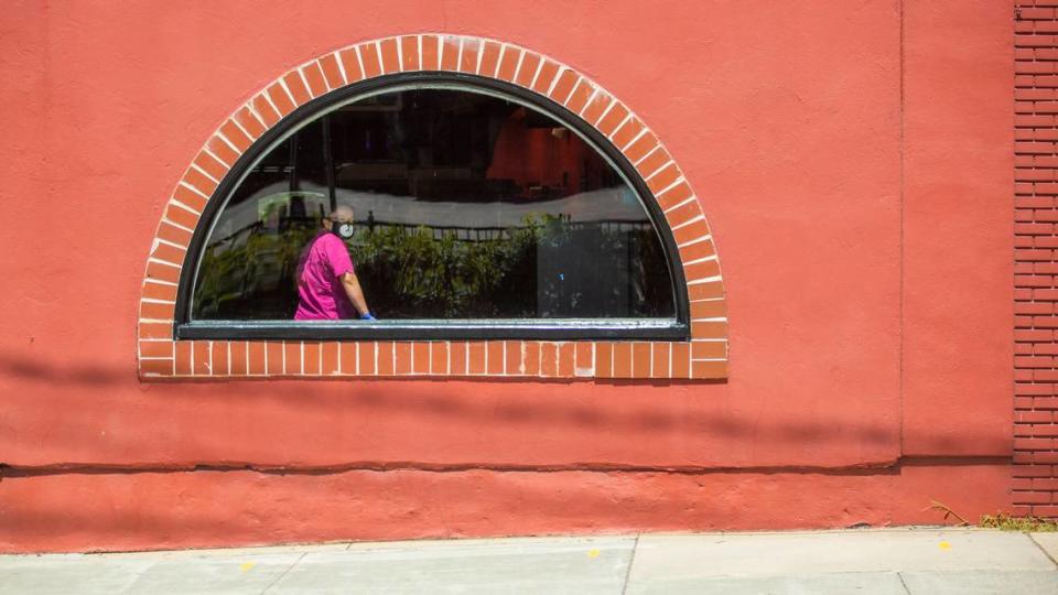 A masked and gloved worker looks outside the window at Torero’s Restaurant as the joint Durham City and County stay-at-home order is announced to be extended past its Friday expiration date, on Tuesday, May 12, 2020, in Durham, N.C.