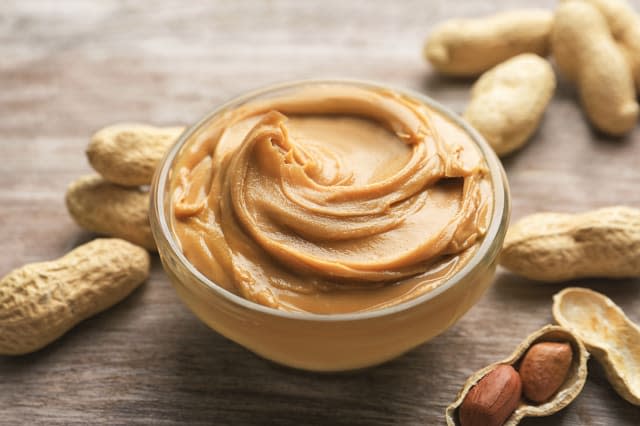 Glass bowl with peanut butter on wooden background