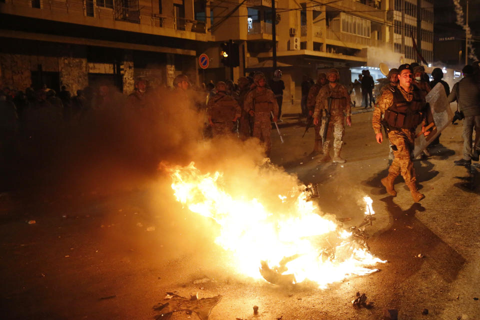 Lebanese army soldiers stand near a motorcycle that was set on fire by protesters, during a clash between supporters of the Shiite Hezbollah and Amal groups and the anti-government protesters, in Beirut, Lebanon, early Monday, Nov. 25, 2019. Security forces fired tear gas amid confrontations in central Beirut that went into Monday morning between Hezbollah supporters and demonstrators protesting against Lebanon's political elite.(AP Photo/Hussein Malla)