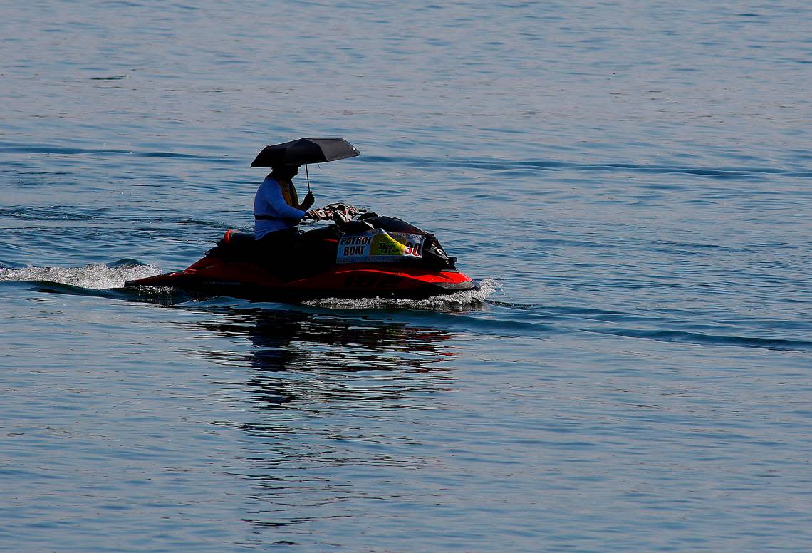 A Water Follies patrol boat driver holds an umbrella for shade while steering the personal watercraft along the Kennewick side of the Columbia River during the first day of the three-day event.