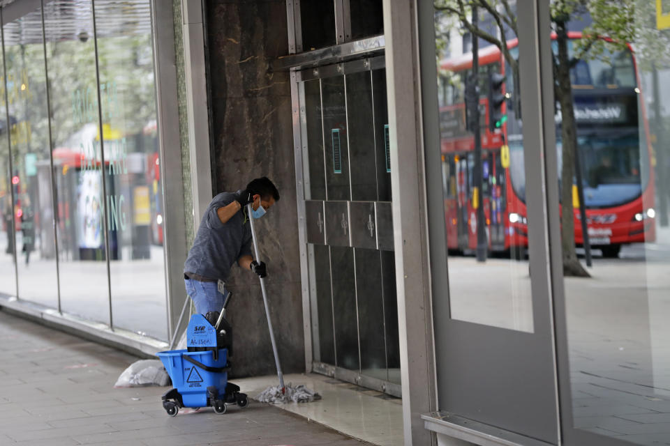 A worker mops a building entrance on Oxford Street in London, Monday, April 12, 2021. Millions of people in England will get their first chance in months for haircuts, casual shopping and restaurant meals on Monday, as the government takes the next step on its lockdown-lifting road map. (AP Photo/Kirsty Wigglesworth)