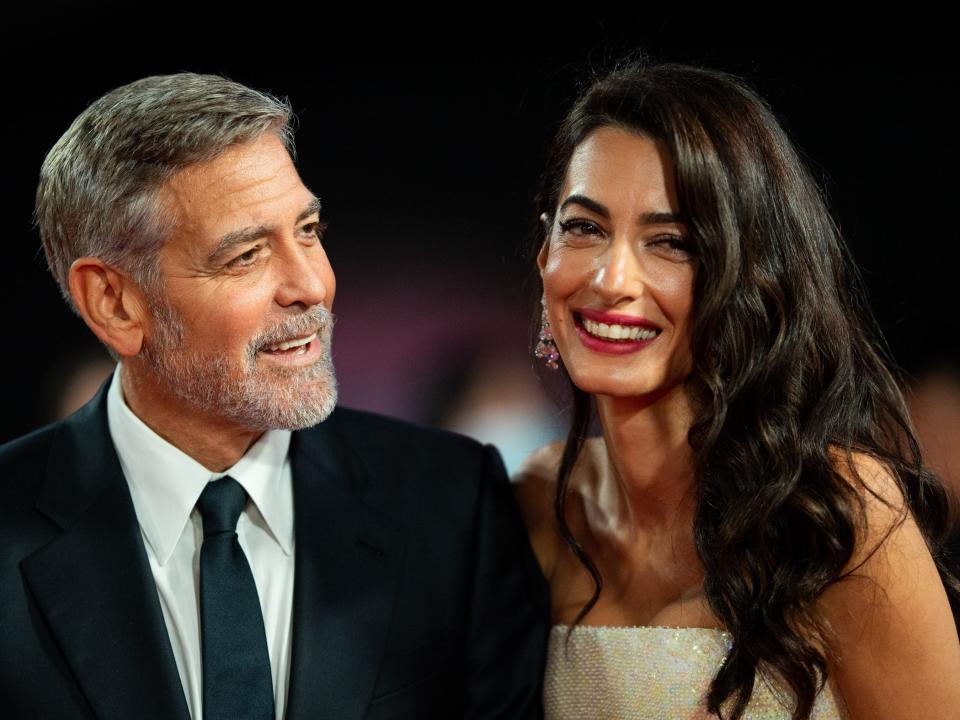 George Clooney in a suit with a black tie and Amal Clooney in a cream strapless dress