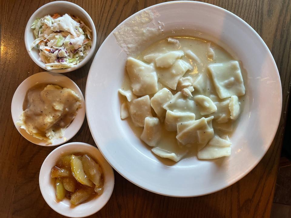 Chicken and dumplings with smaller bowls of coleslaw, mashed potatoes, and fried apples