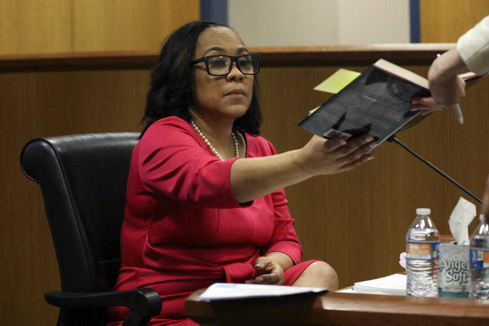 Fulton County District Attorney Fani Willis is is handed the book "Find Me the Votes", to read over a quote from herself as she testifies during a hearing on the Georgia election interference case, Thursday, Feb. 15, 2024, in Atlanta. The hearing is to determine whether Willis should be removed from the case because of a relationship with Nathan Wade, special prosecutor she hired in the election interference case against former President Donald Trump. (Alyssa Pointer/Pool Photo via AP)