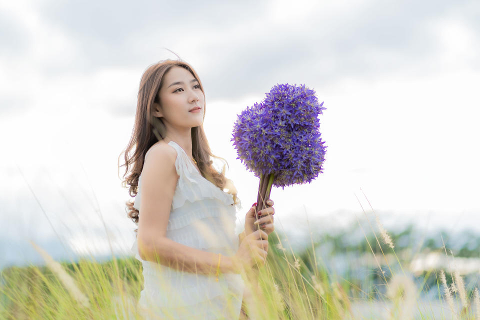 Beautiful Asian woman holding purple bouquet in flower garden, Chiang Mai, Thailand, holiday travel concept.