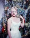 <p>Film star Lana Turner dazzles in a white gown while standing in front of an equally glitzy Christmas tree. </p>