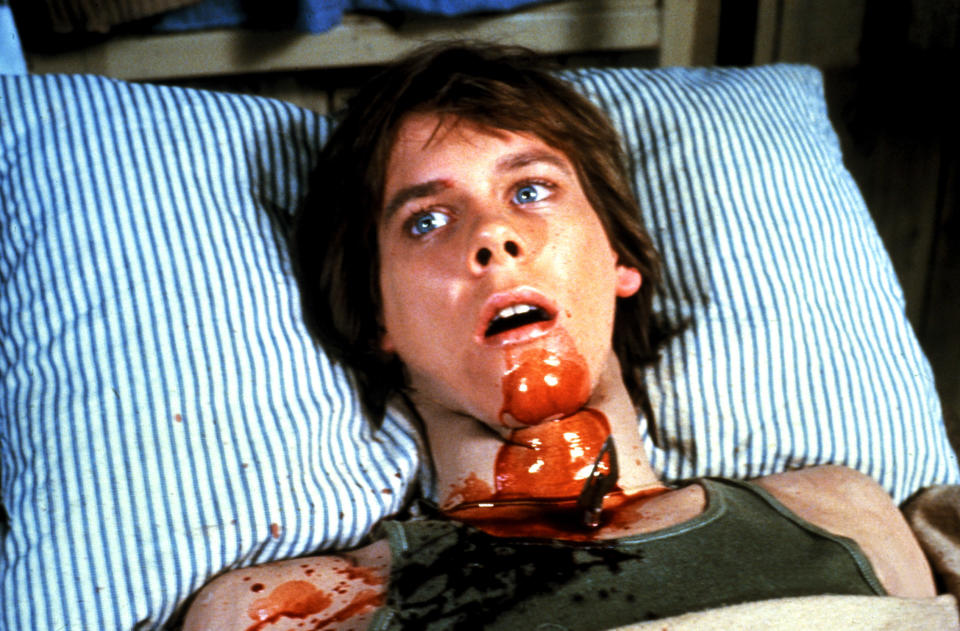 Kevin Bacon laying in bed and covered in blood.