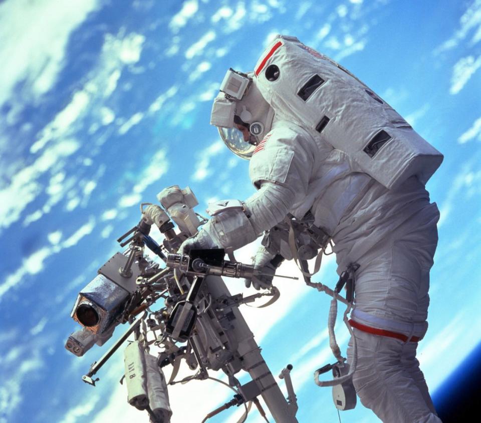 STS103-701-047 (19-27 December 1999) --- Astronaut Steven L. Smith, payload commander, retrieves a power tool while standing on the mobile foot restraint at the end of the remote manipulator system (RMS). Many of the tools required to service the Hubble Space Telescope are stored on the handrail attached to the RMS visible in the photograph.  