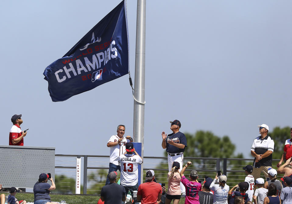 Atlanta Braves manager Brian Snitker, center right, looks up at World Series Champions flag as it is hoisted in center field at CoolToday Park before a spring training baseball game against the Minnesota Twins Friday, March 18, 2022, in North Port, Fla. (Curtis Compton/Atlanta Journal-Constitution via AP)