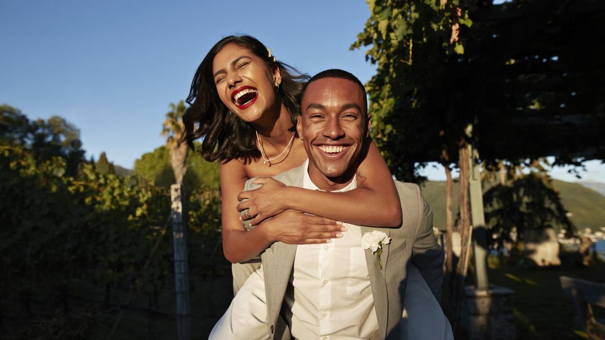 happy groom piggybacking laughing bride in vineyard