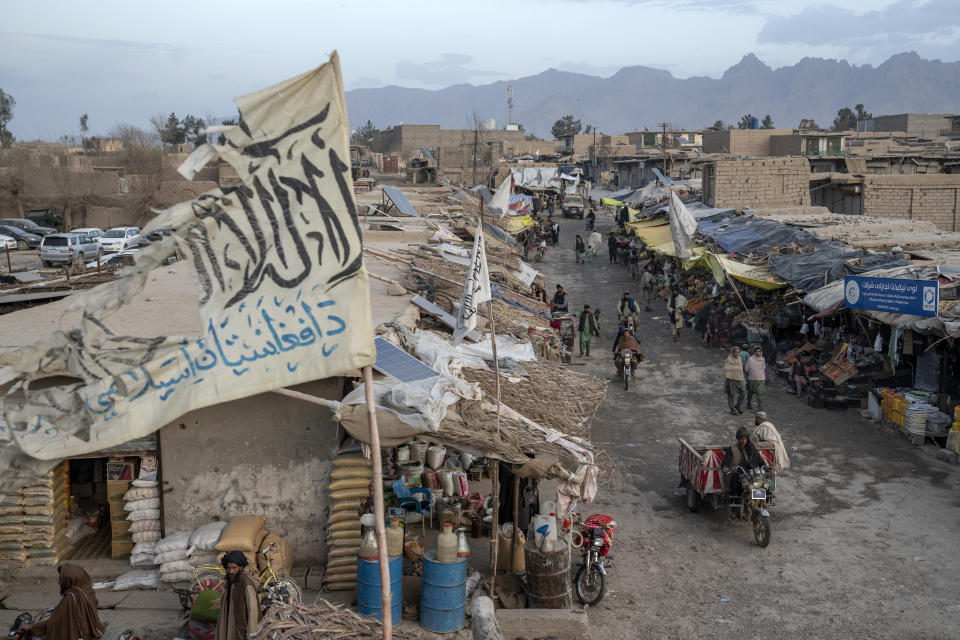 People walk through a market with old Taliban flags flown above in a town in a remote region of Afghanistan, on Saturday, Feb. 25, 2023. In a nearby village, a baby was orphaned during a U.S. raid in 2019. A Marine who adopted her claims her parents were foreign fighters. But villagers say they were innocent farmers caught in the fray. (AP Photo/Ebrahim Noroozi)