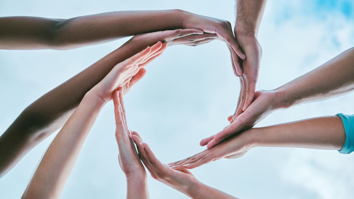  illustration of several people putting their hands in a circle with blue sky and clouds in behind 