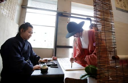 Hai Zhaohang dressed in "Hanfu" signs a guestbook as he arrives to attend a performance of the "guqin" traditional musical instrument in Beijing, China