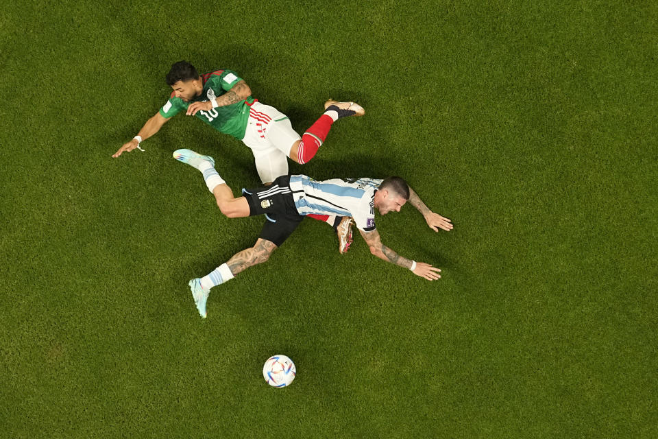 Mexico's Alexis Vega, top, falls to the ground in a clash with Argentina's Rodrigo De Paul during the World Cup group C soccer match between Argentina and Mexico, at the Lusail Stadium in Lusail, Qatar, Saturday, Nov. 26, 2022. (AP Photo/Pavel Golovkin)